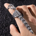 A silver-toned gothic skeleton ring designed like a dagger, shown worn on a person's finger against a textured black background.